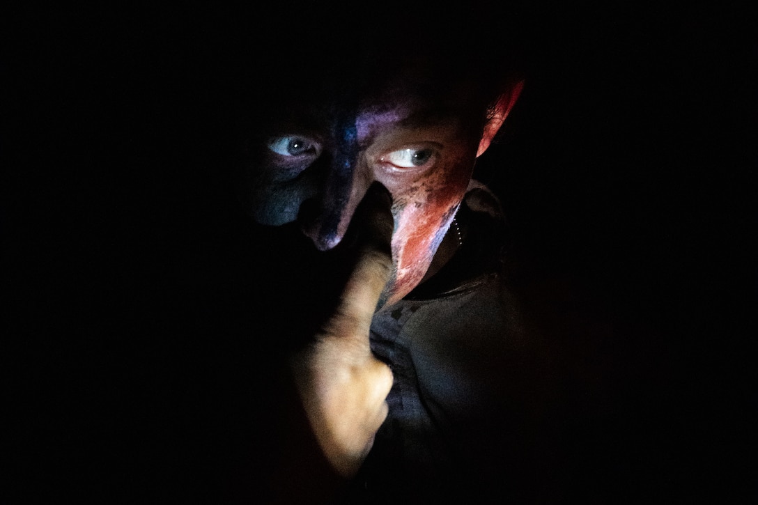 A Marine applies camouflage around the eyes while surrounded by darkness.