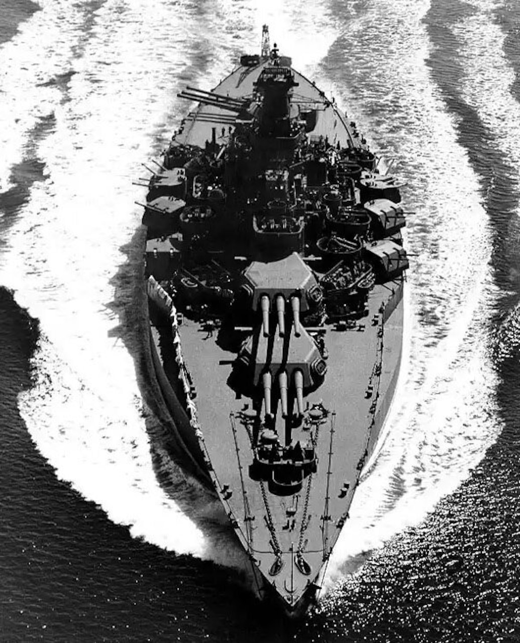 A Battleship makes waves as it sails through the ocean in a black and white photo.