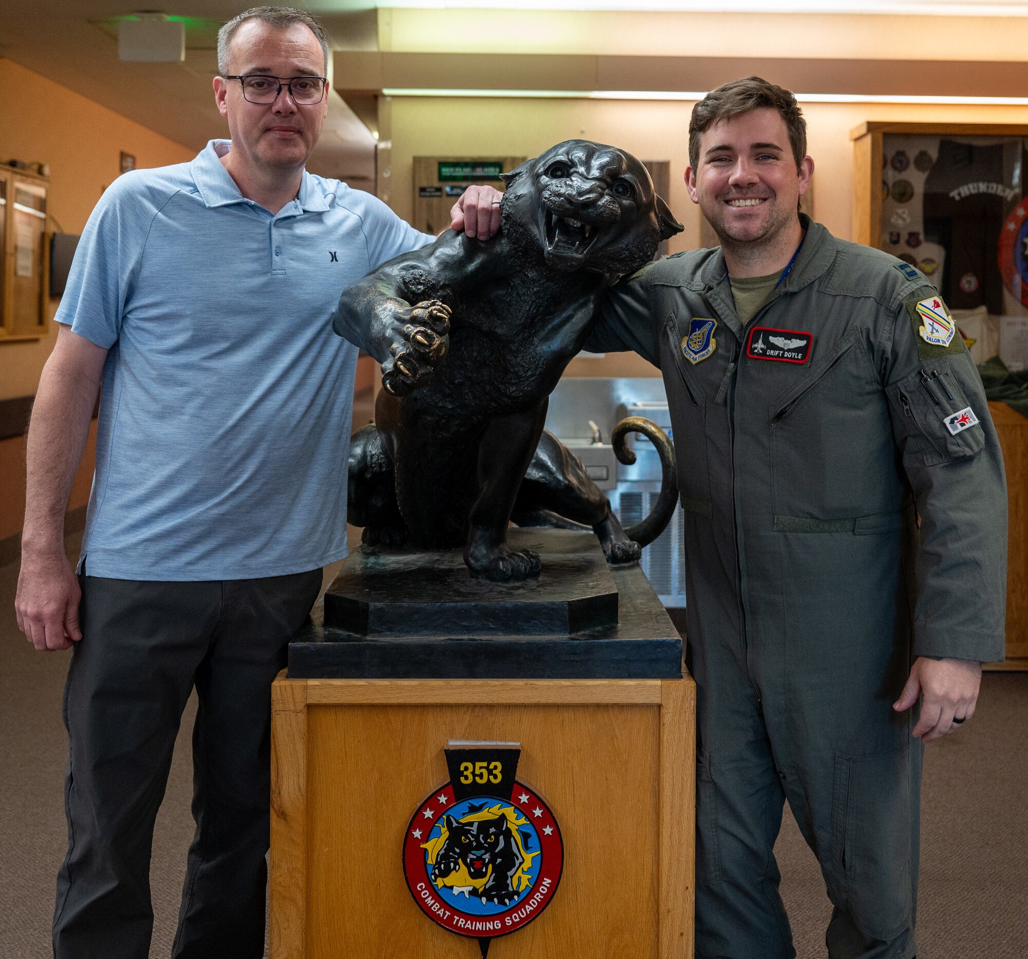 Two members from the 353rd Combat Training Squadron stand on either side of a black panther statue with the 353rd CTS emblem.