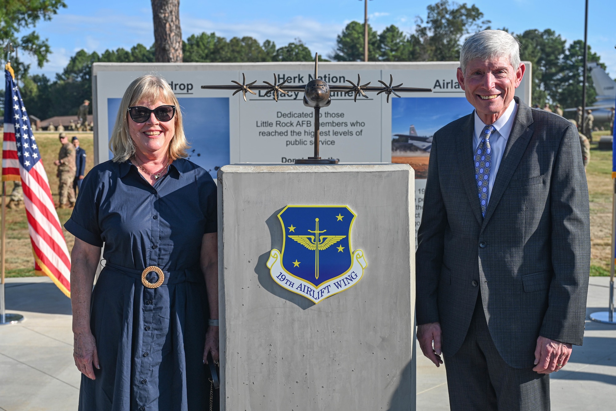 A woman and a man stand next to a podium with a small, bronze C-130J Super Hercules aircraft statue on it.