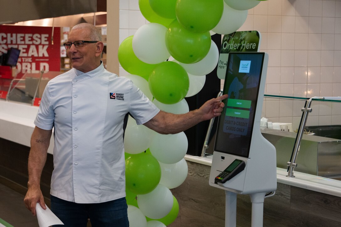 Robert Irvine pointing at self-service kiosk.