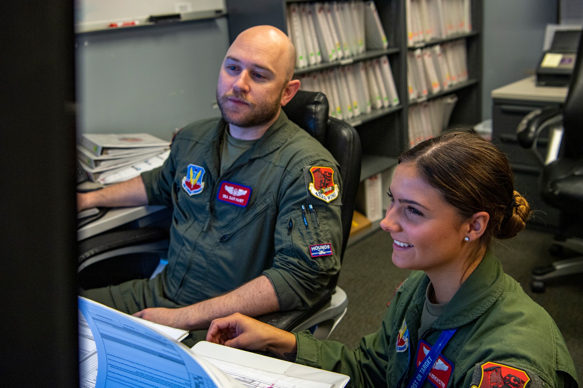 A man and a woman in flight suits work at an office.