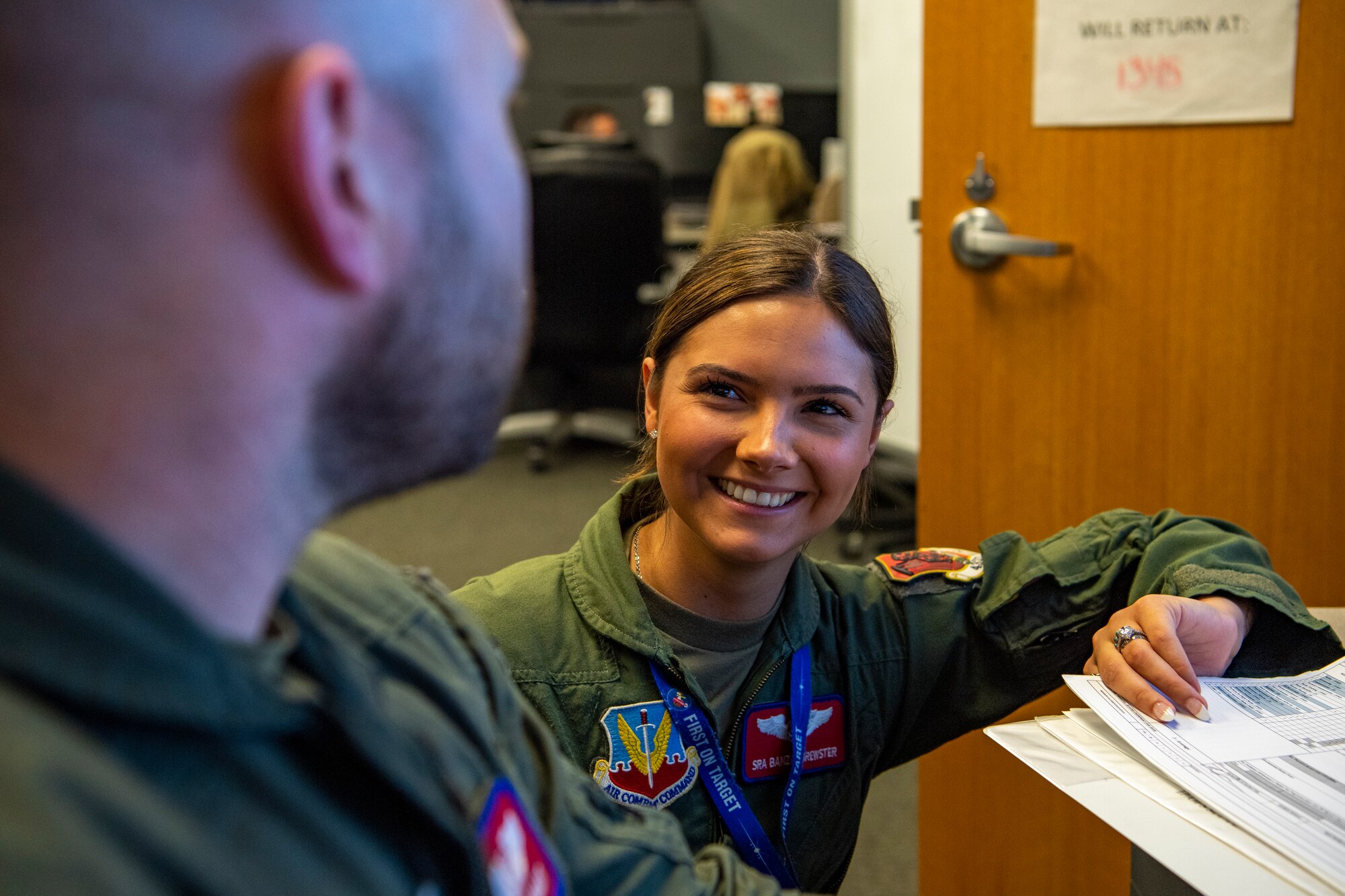 A woman in a flight suit smiles in an office.