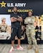 Man and female soldier stand in front of a banner with photos and U.S. Army logo.