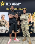 Man and female soldier stand in front of a banner with photos and U.S. Army logo.