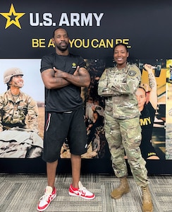 Man and female soldier stand in front of a banner with photos and U.S. Army logo.