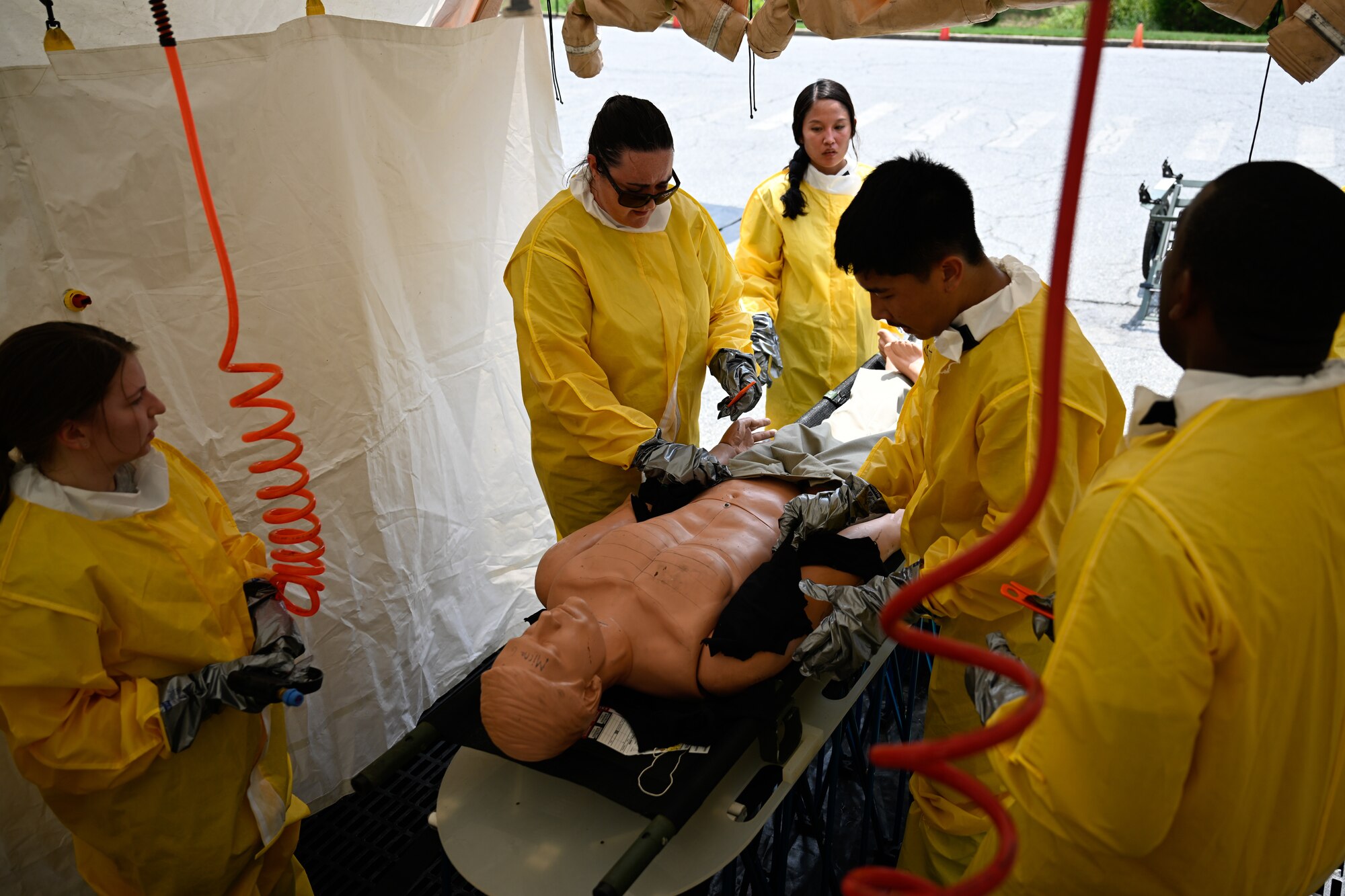 Airmen cut away clothing on a mannequin during a decontamination exercise.