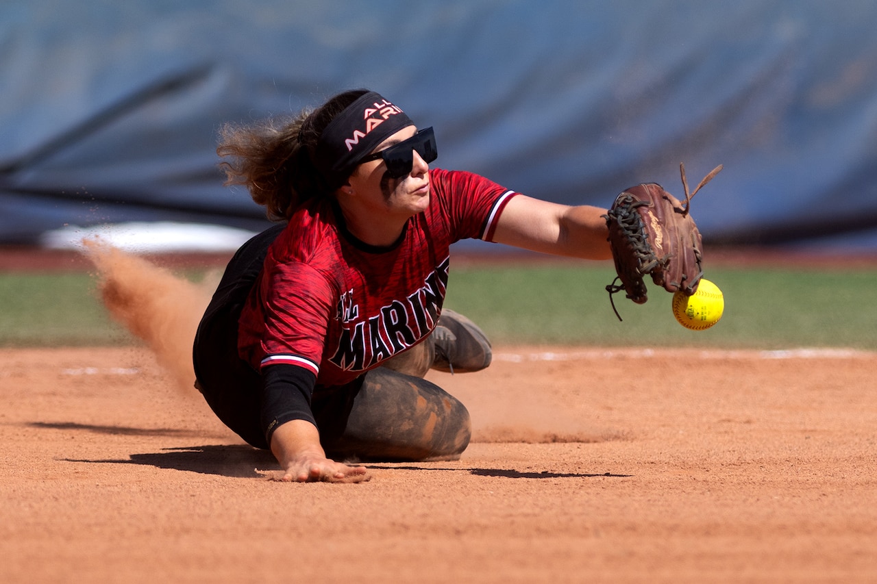 A softball player falls to the ground to knock a ball out of the air.