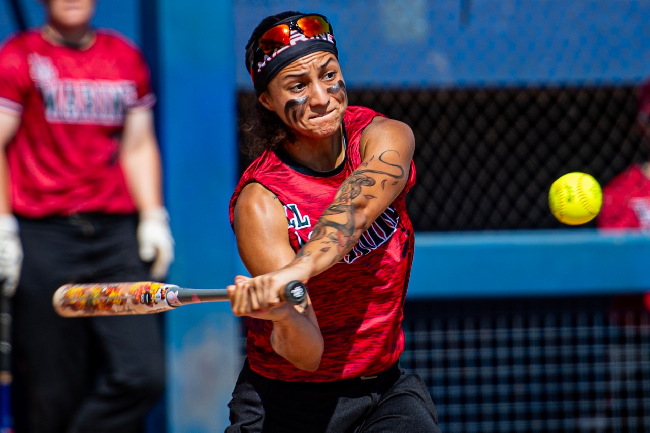 A softball player holding a bat focuses on a ball.