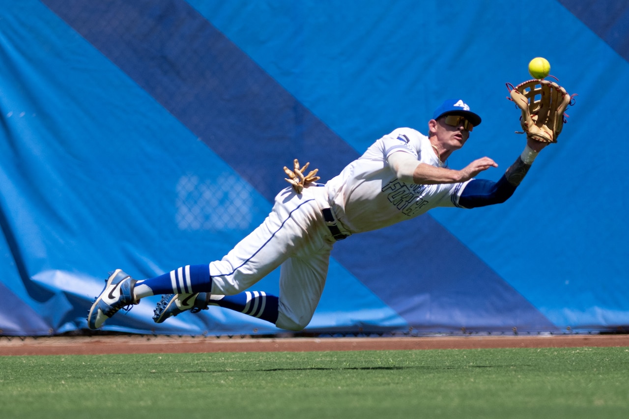 A softball player makes a catch before falling to the ground.