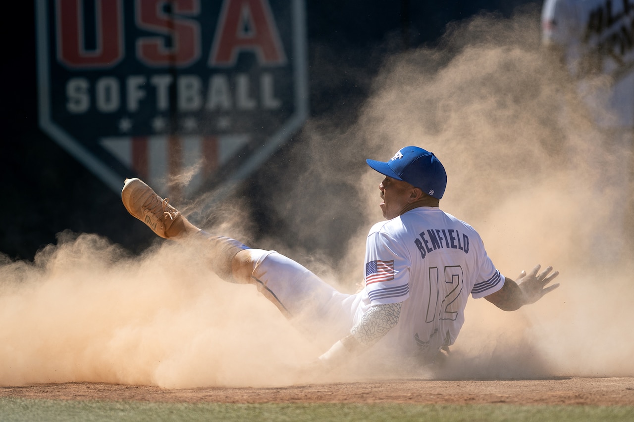 A softball player slides into home plate in a cloud of dust.
