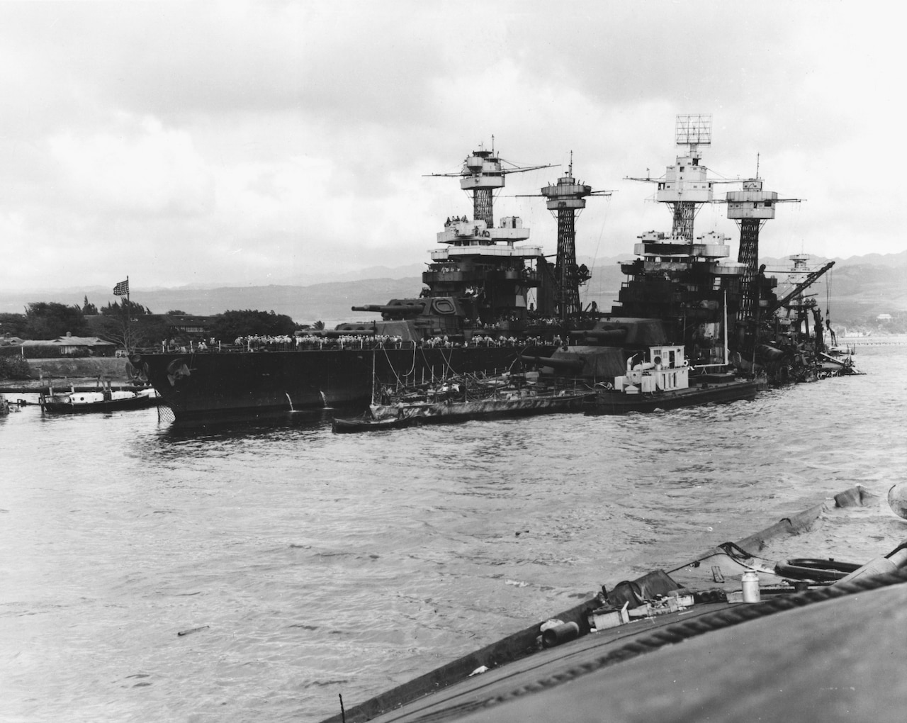 Two damaged battleships are moored in a harbor.