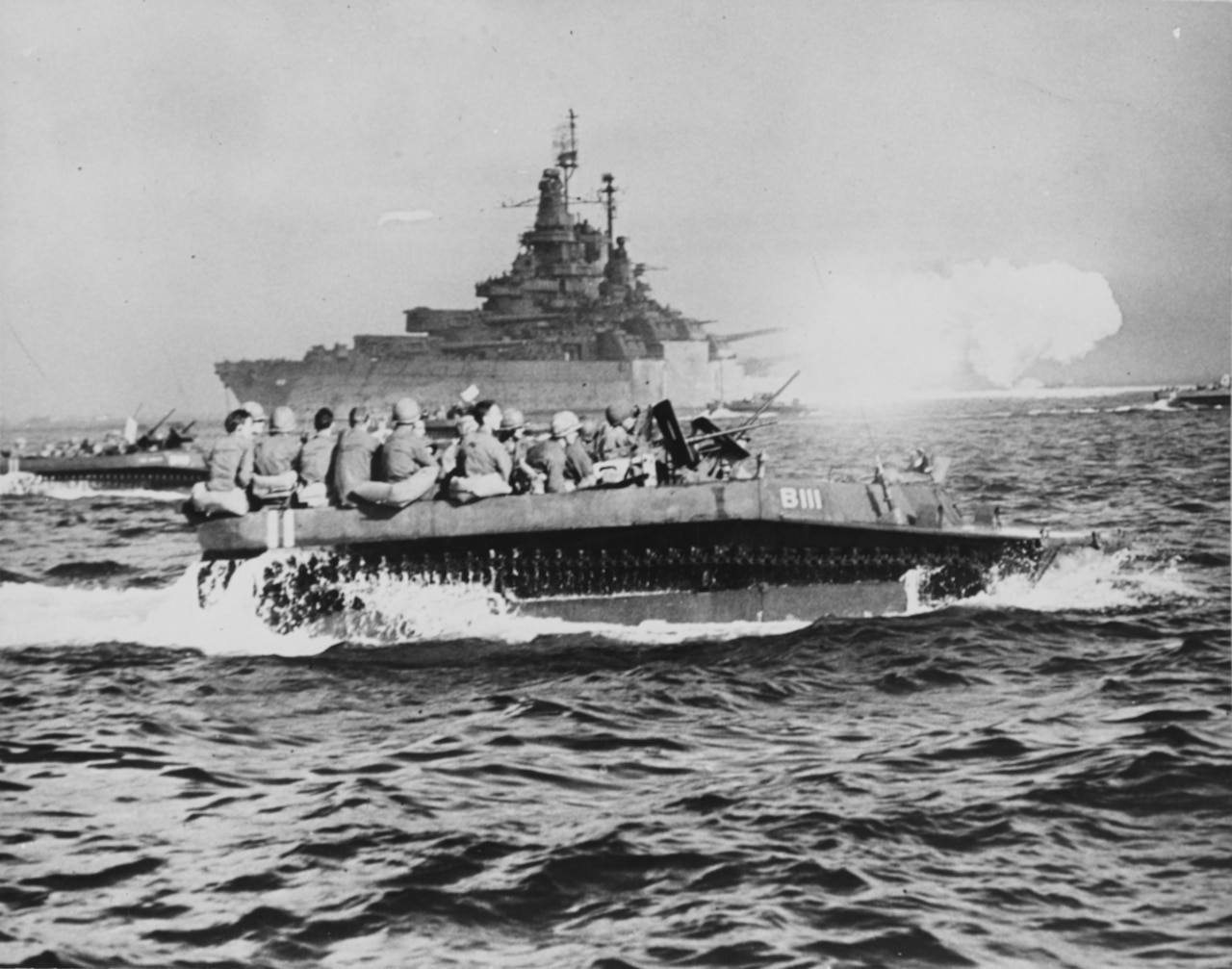 Battleships’ guns blaze as troops in small boats head for shore.