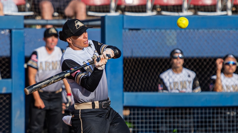 A woman wearing a softball uniform holds a bat and prepares to swing at a softball.