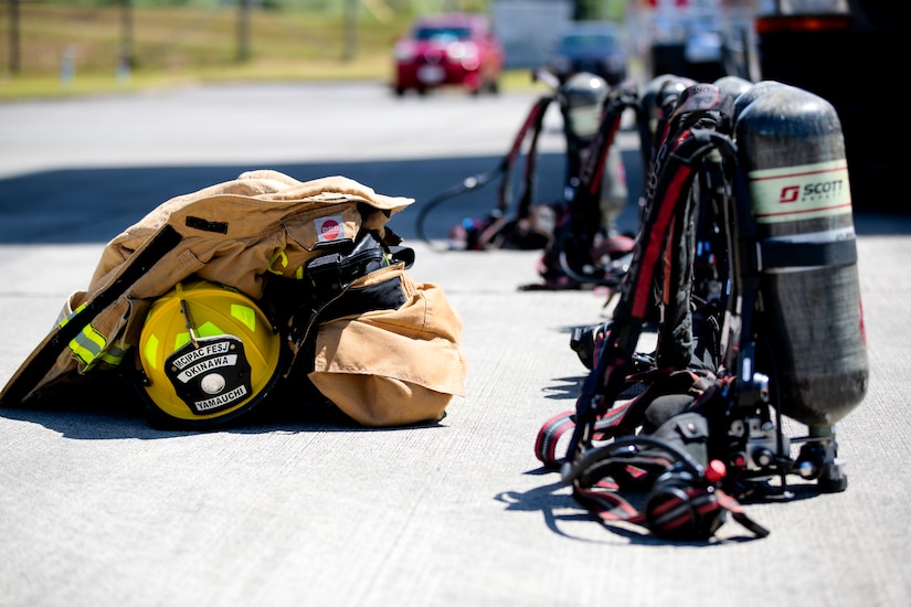 A row of oxygen tanks are staged near a firefighter helmet and suit.