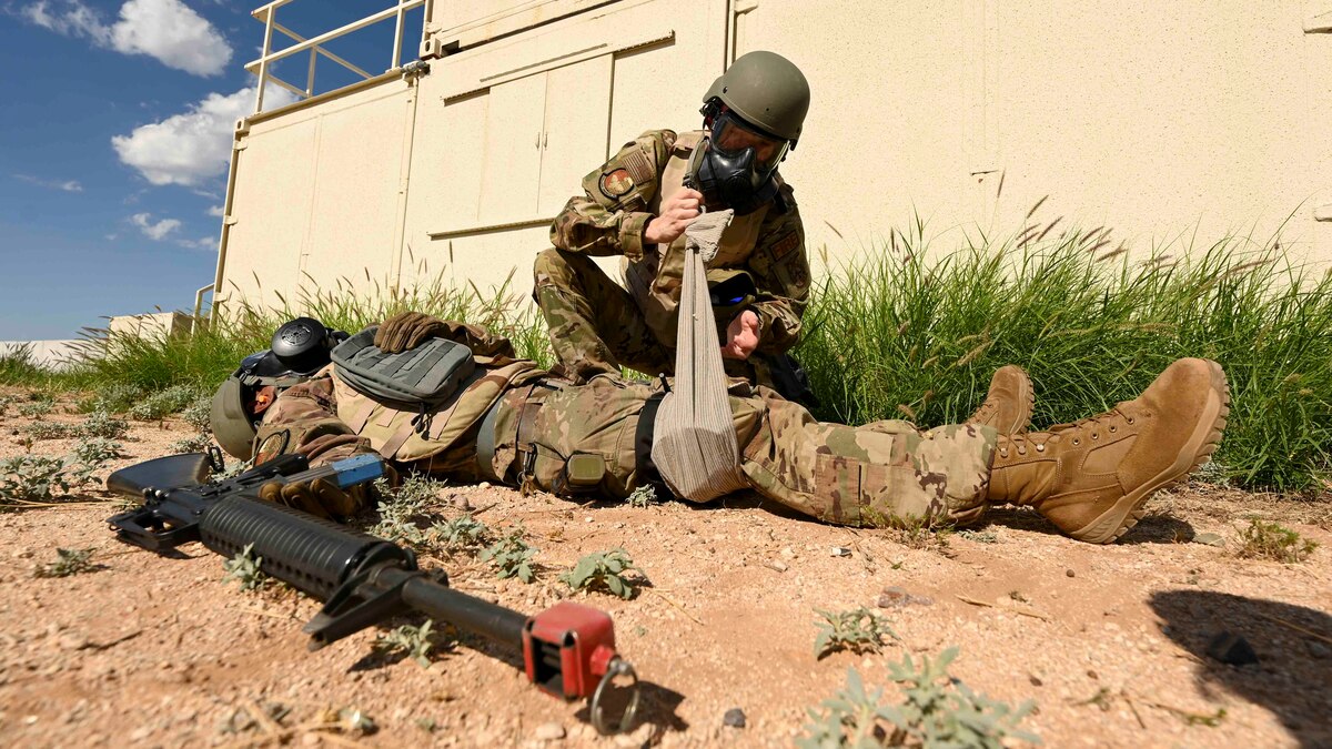 A man in a military uniform bandages the leg of another man.