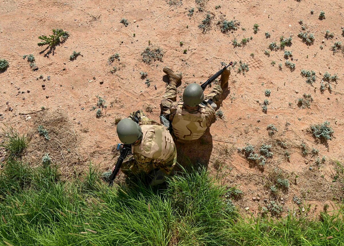 People in military uniforms sit back to back on the ground