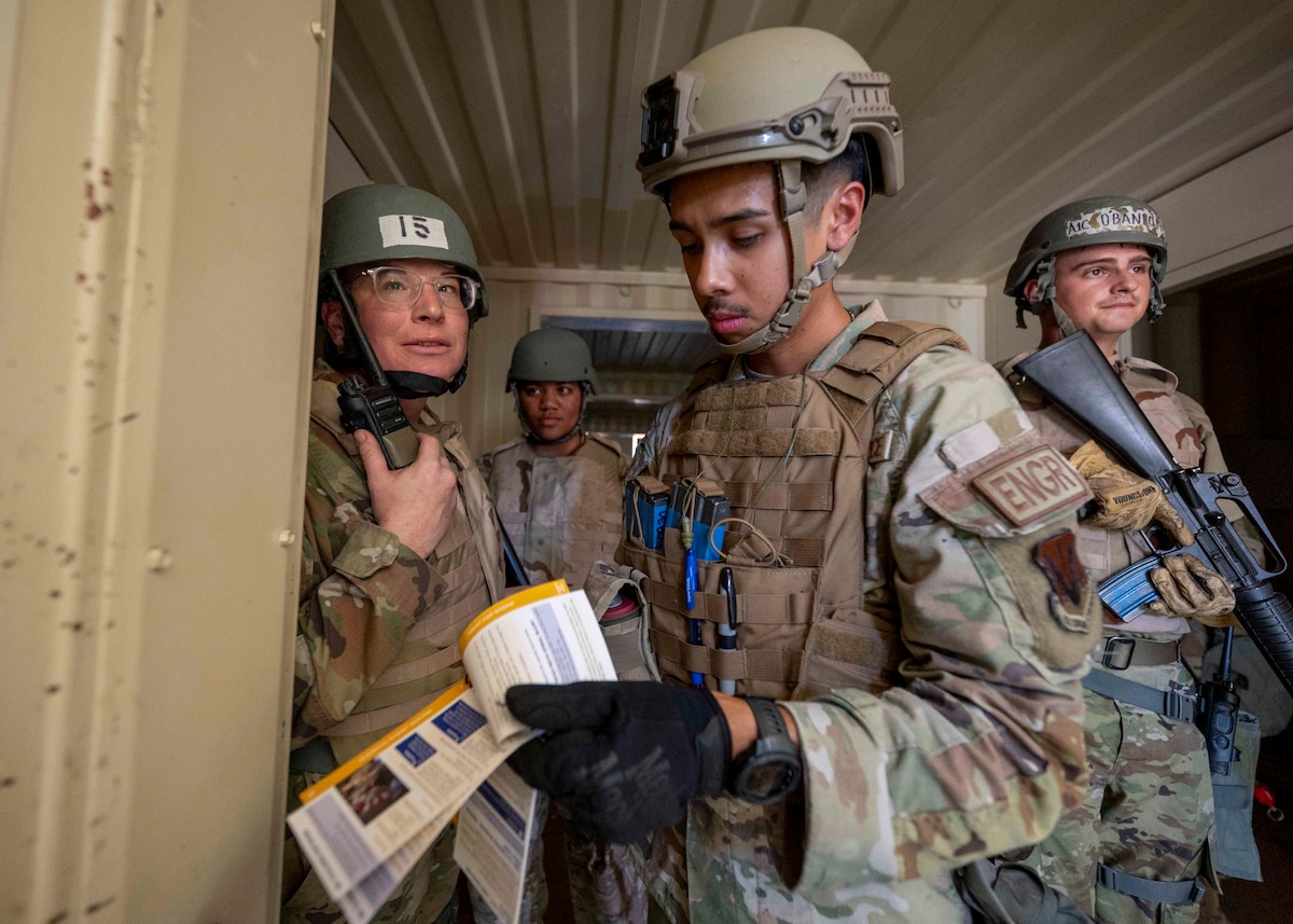 People in military uniforms use a handheld radio.