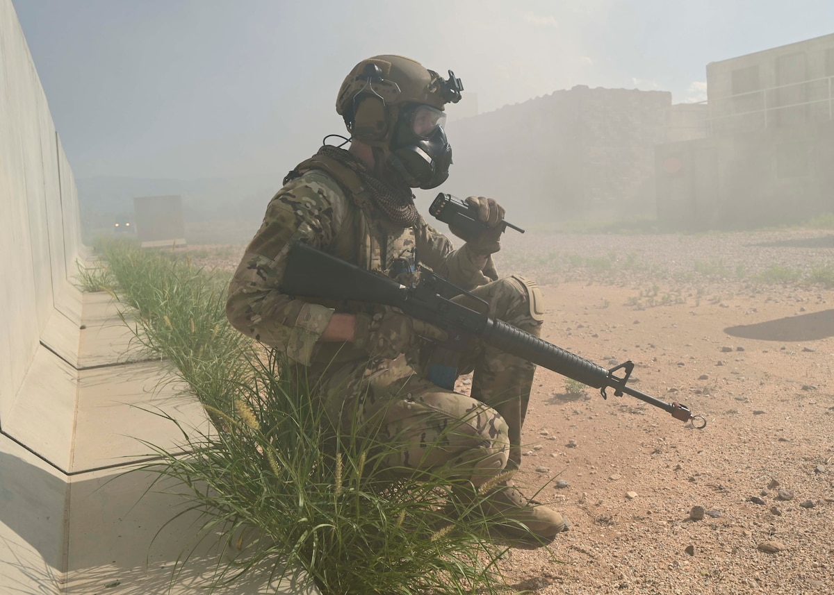 A man in a military uniform with a rifle uses a handheld radio