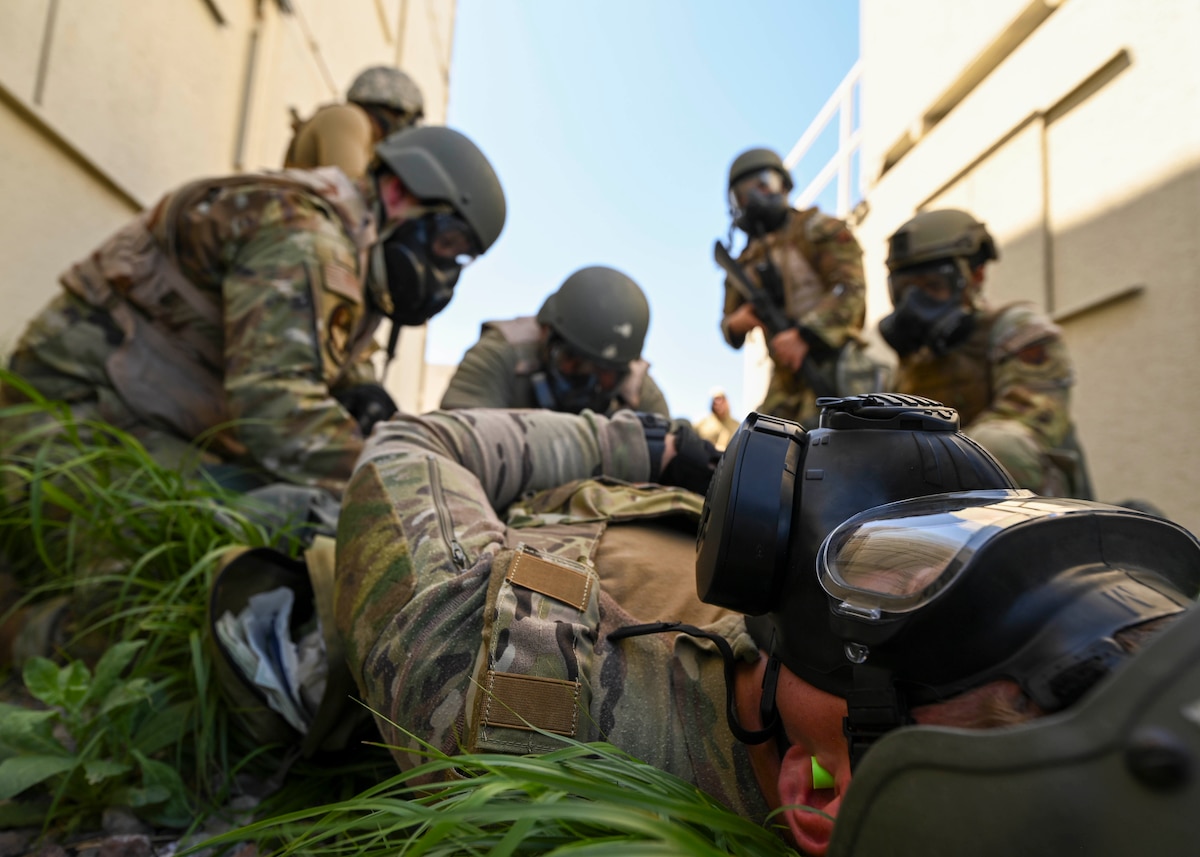 People in military uniforms and gas masks stand over an injured man.