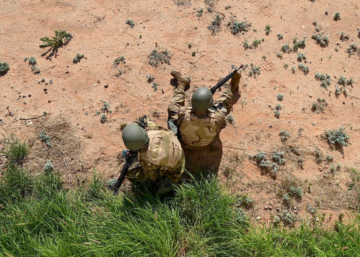 People in military uniforms sit back to back on the ground