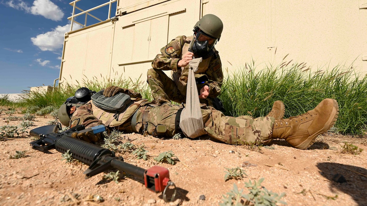 A man in a military uniform bandages the leg of another man.