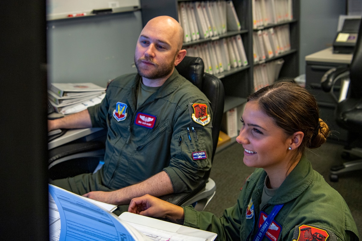 A man and a woman in flight suits work at an office.
