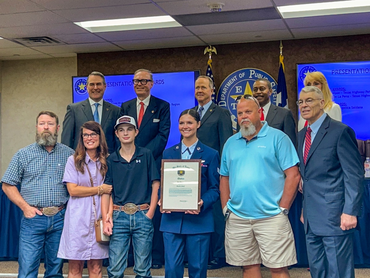 A woman in a military uniform holds a certificate surrounded by her family and Texas officials.