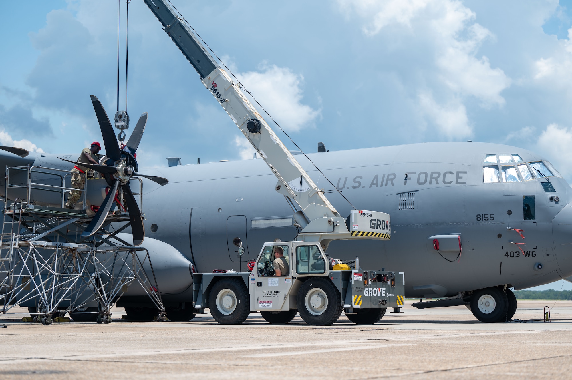 A crane hoists a propeller into place to be installed onto a C-130j