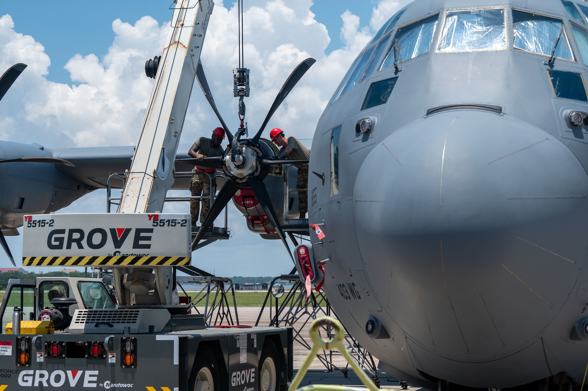 A crane hoists a propeller in place as Airmen install it onto a C-130j
