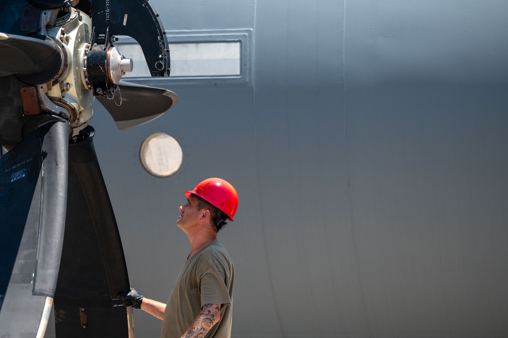A propeller fills the left side of the frame and to the right an Airman stands holding onto it to keep it steady