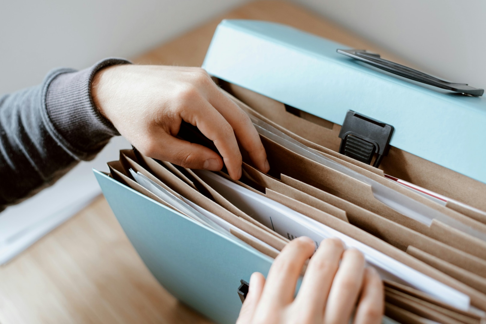 Two hands search through manila folders in file cabinet.