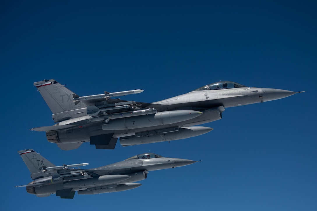 Two military aircraft fly overhead during daylight.