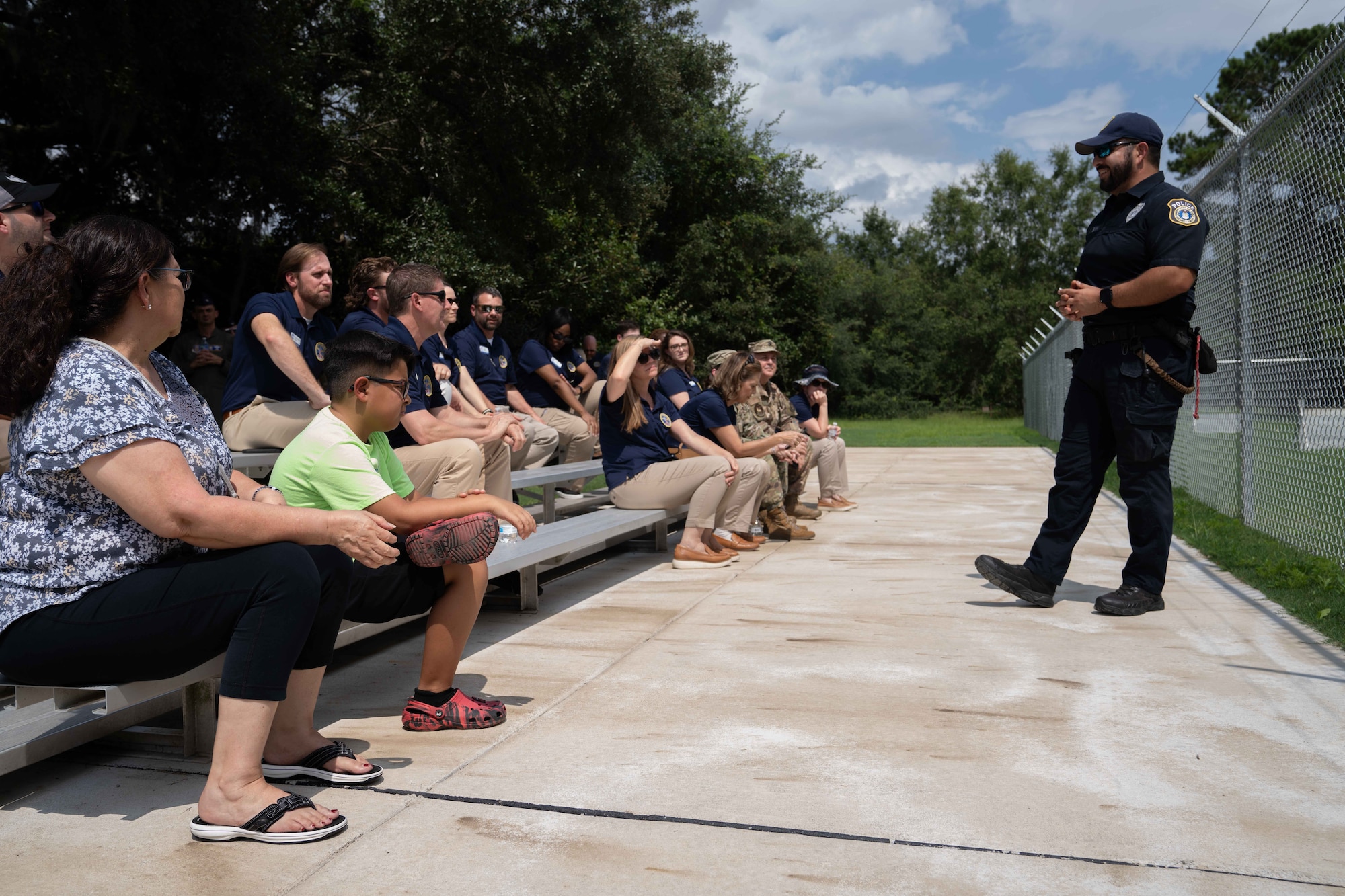 Civic leaders sit of bleachers listening as a member of the 628th Security Forces Squadron prepares them for a military working dog demonstration.