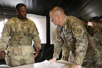 Lieutenant General Hale leans onto a map board while listening to an Army officer describe the situation.