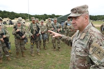 Lieutenant General Hale, at the right of the image, addresses a group of uniformed soldiers. His hand is outstretched as he speaks.