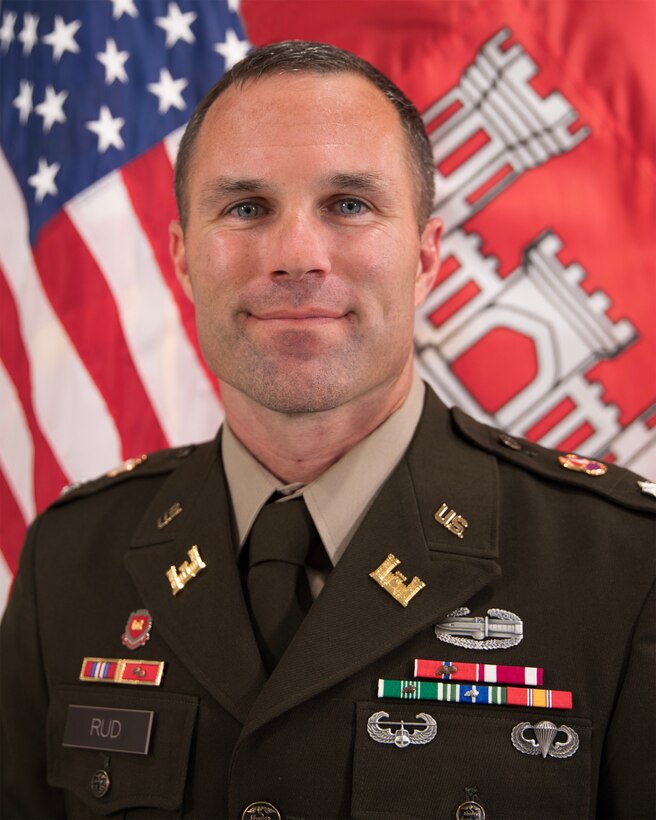 A man in a military uniform in front of the United States flag and the U.S. Army Corps of Engineers flag.