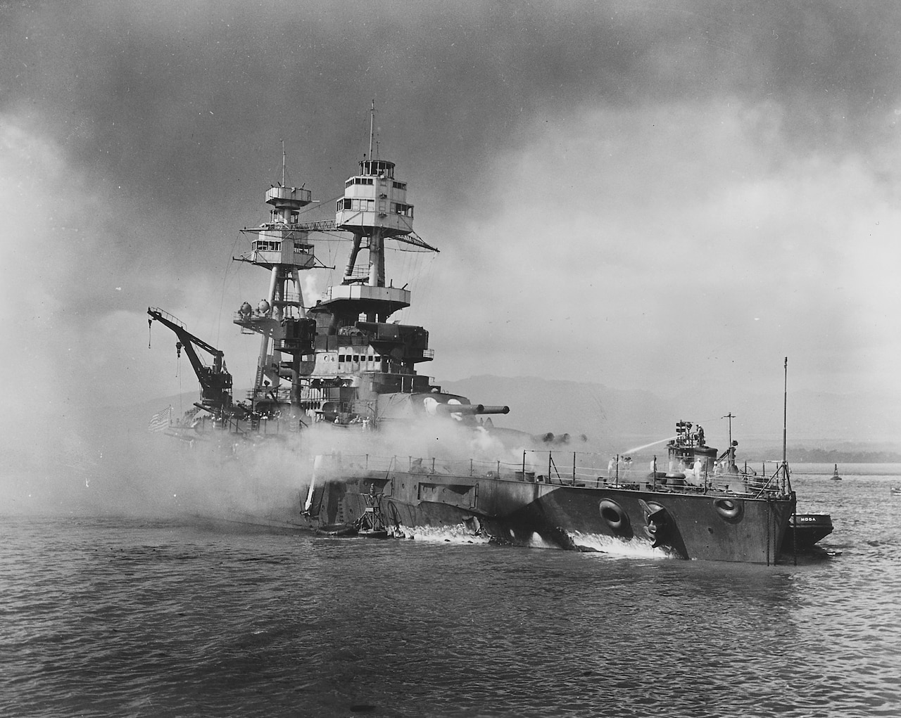 A battleship at sea is sinking with smoke pouring out.