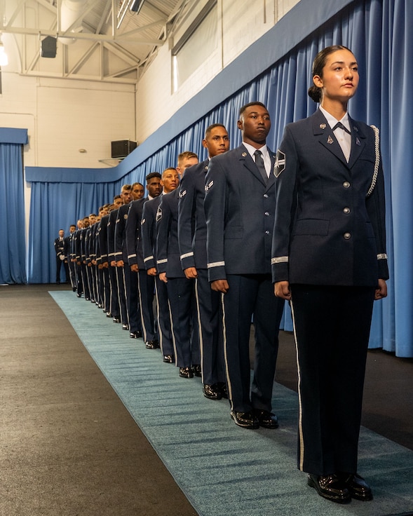 Six U.S. Space Force Guardians and 12 U.S. Air Force Airmen stand in a single file during a graduation ceremony