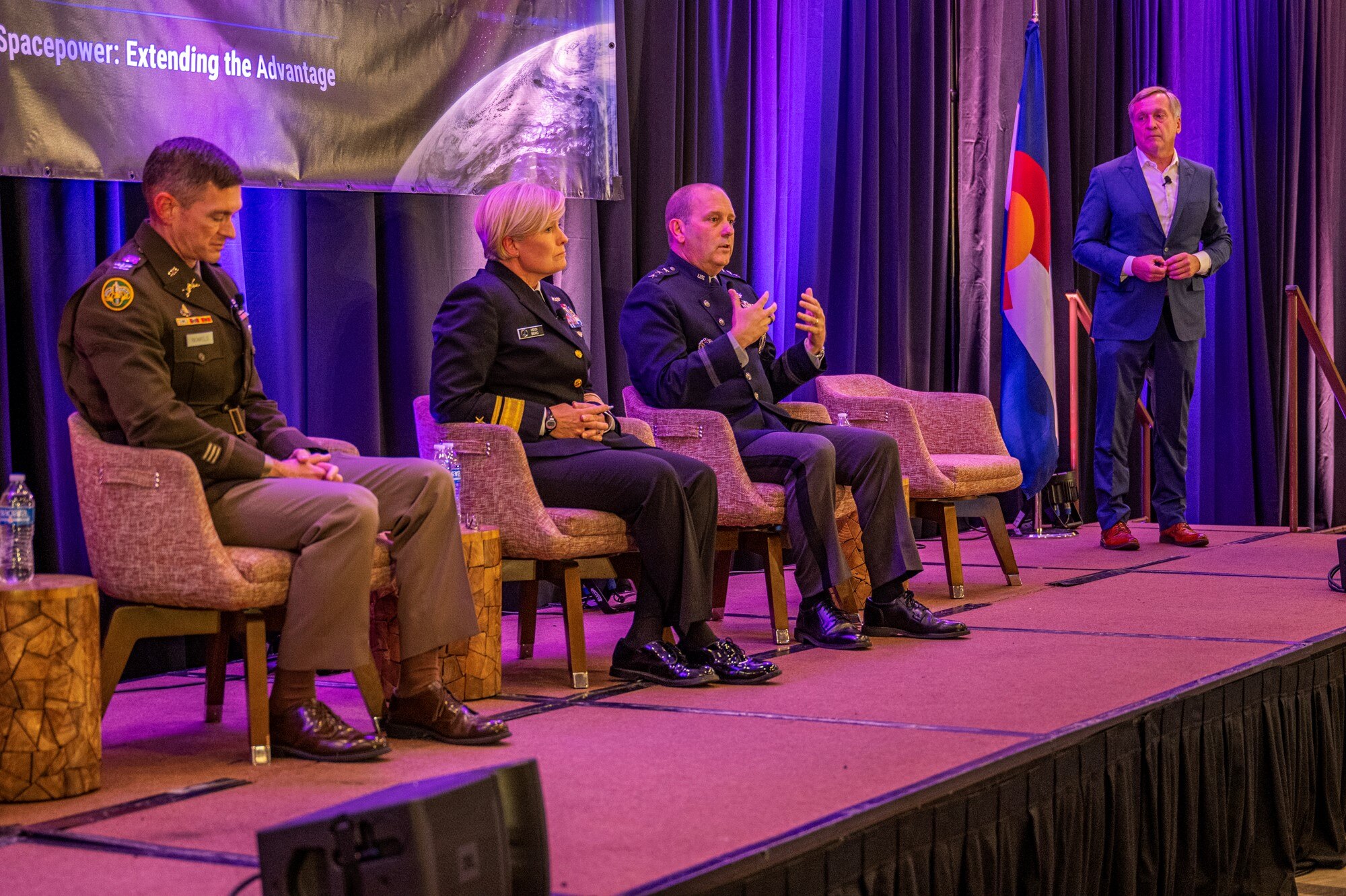 Three senior military officers speak at a forum, with a moderator.