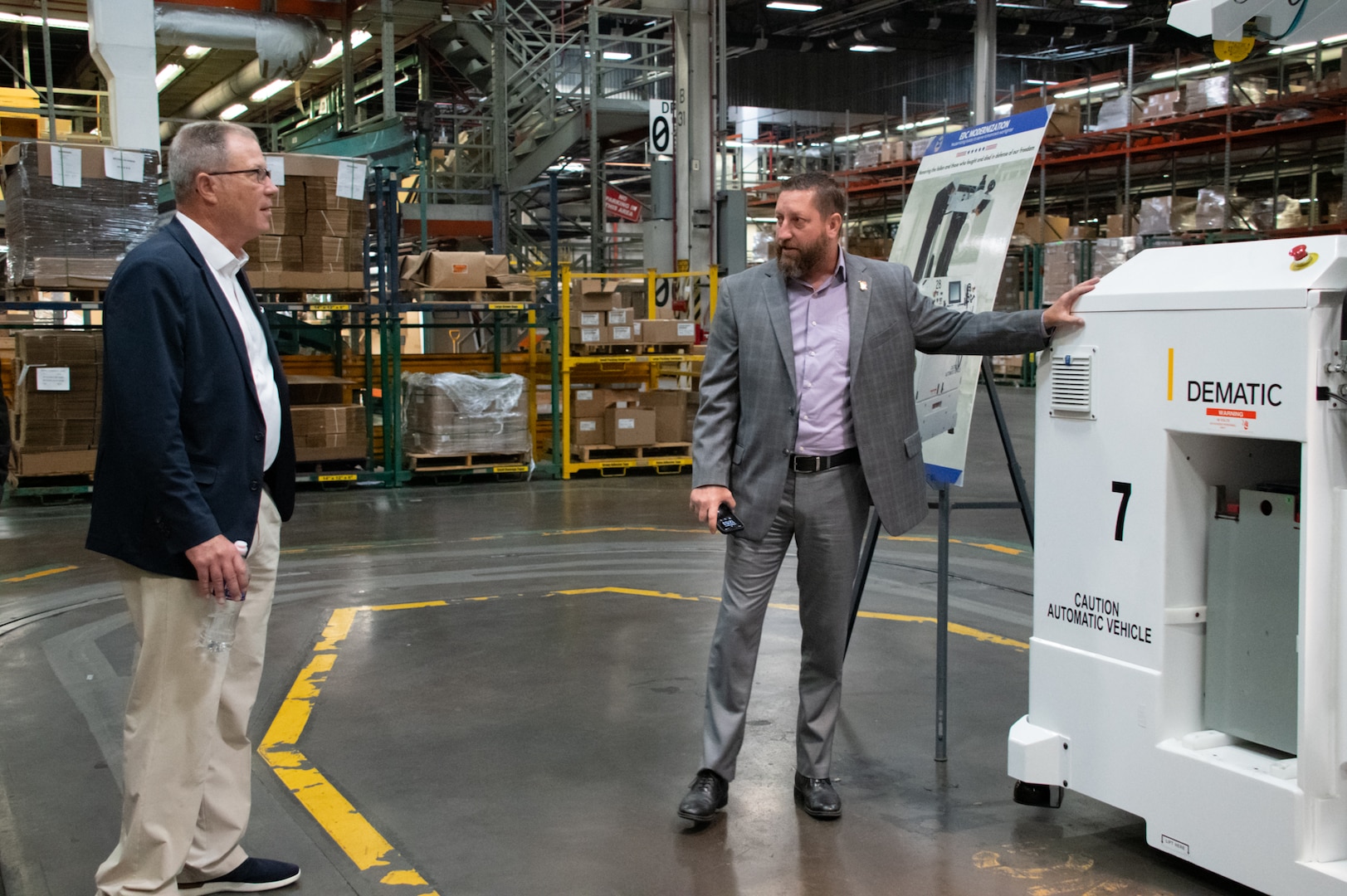 Two men talk as one points to a piece of warehouse equipment