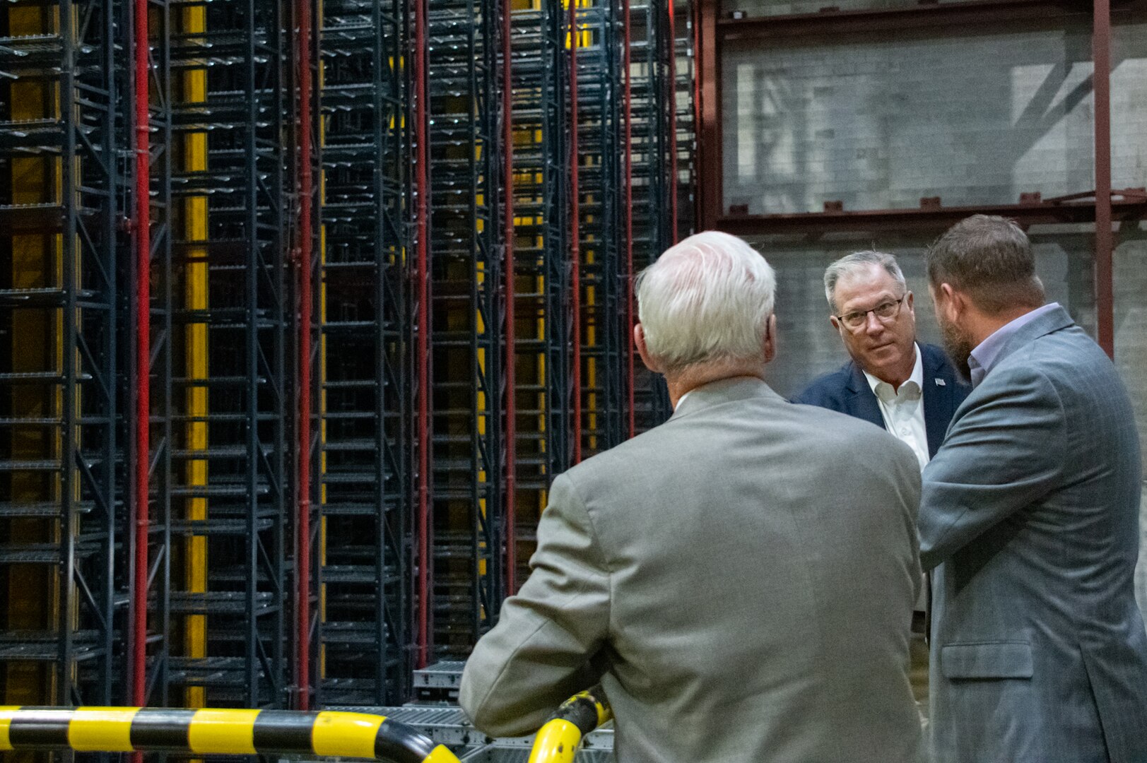 Three men in suits talking in an industrial warehouse.