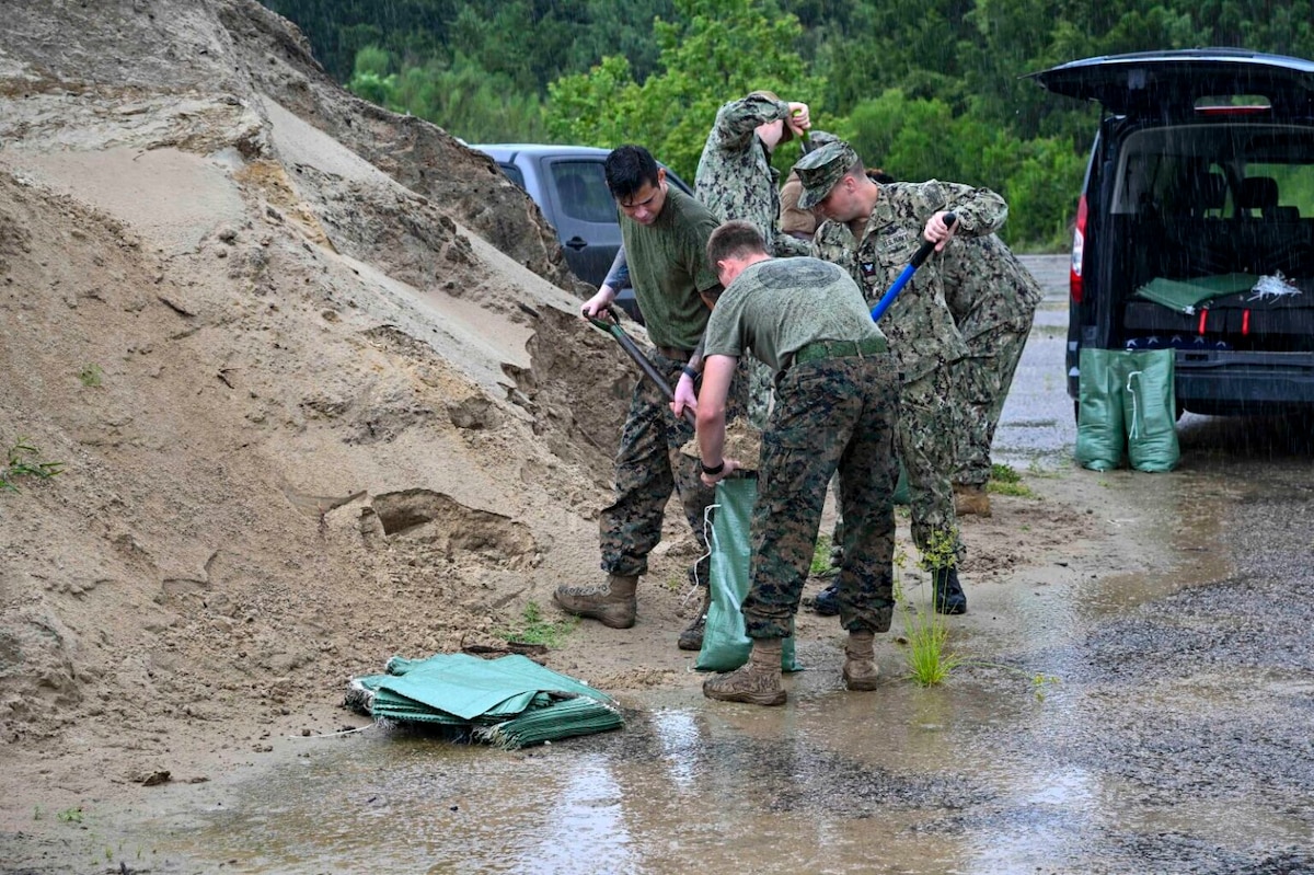 Uniformed service members shovel sand into bags.
