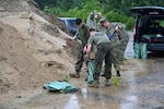 Uniformed service members shovel sand into bags.
