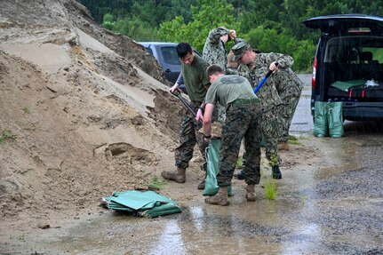 Uniformed service members shovel sand into bags.