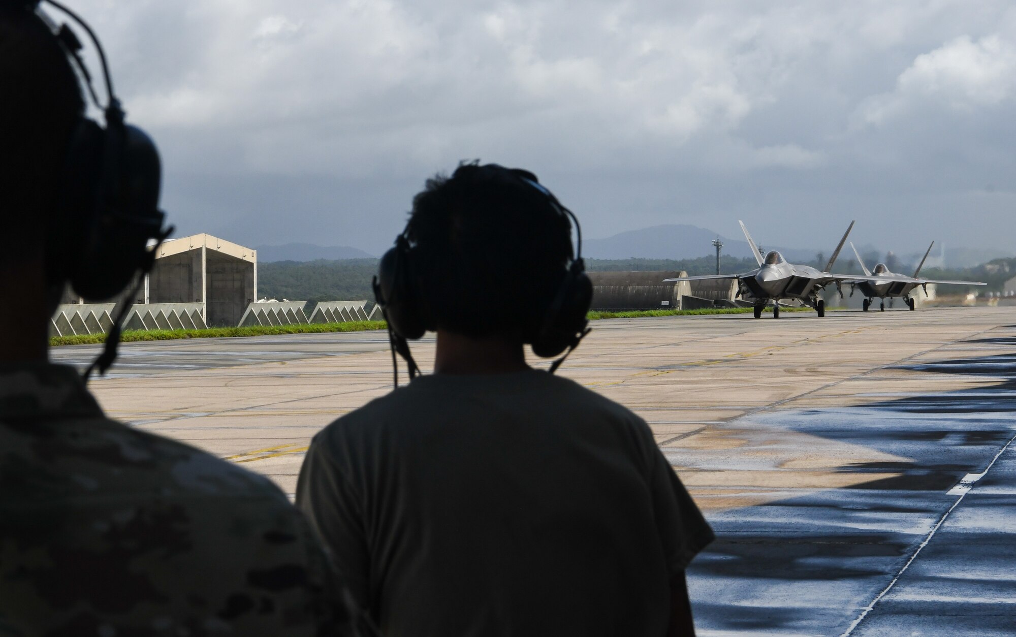 Two Airmen watch two F-22 Raptors taxi back to a hangar.