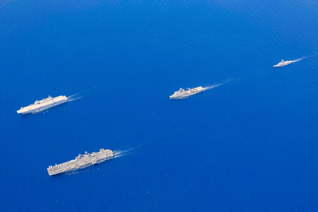 Four military ships steam in formation across a dark blue ocean.