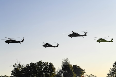 Four Army helicopters fly over a tree line