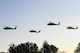 Four Army helicopters fly over a tree line