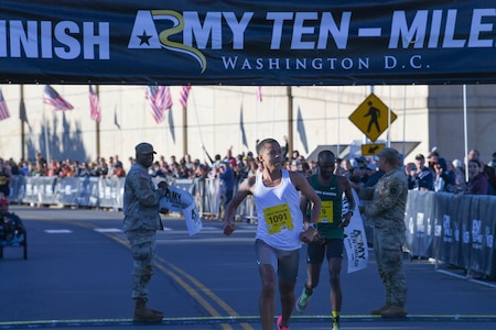 Two runners cross the finish line during a race. There is a banner above the finish line with the words Army Ten-Miler.